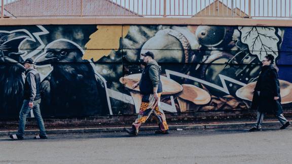 Three people walking against a backdrop of a raven graffiti mural