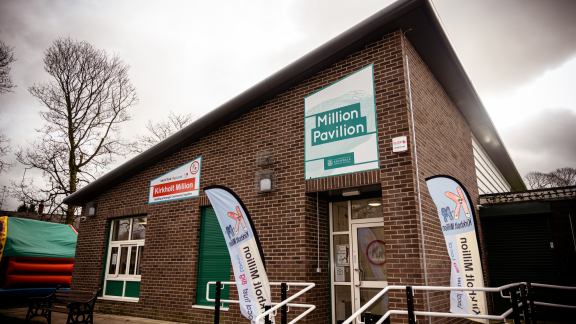 A wide-angle view of a single-storey red-brick building with a sign reading 'Million Pavilion' above the door.