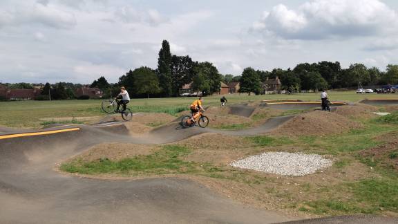 An undulating concrete bike track with bunkers on a sandy, grassy area with trees in the background.