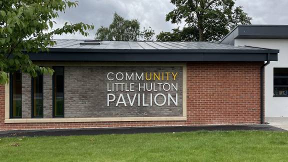 One-storey red bricked building with grey sloping roof and grey bricked sign reading 'Community Little Hulton Pavilion'