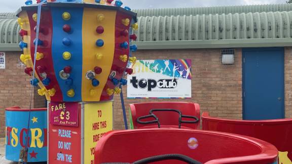 Brightly-coloured fairground rides outside a red-brick building.