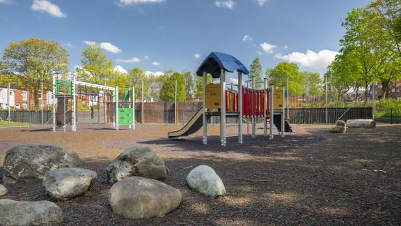 Play equipment including slides on a sunny day, with large feature rocks in the foreground.