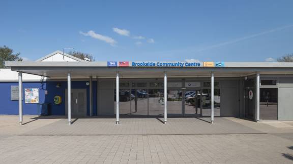 A modern single-storey building with glass windows, with a sign reading "Brookside Community Hub" above the frontage.