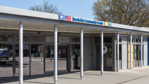 A modern single-storey building with glass windows, with a sign reading "Brookside Community Hub" above the frontage.