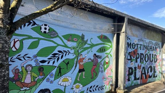 A colourful mural on a concrete wall showing people doing activities on giant plant leaves.