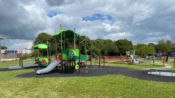 A grassy park area with large play equipment, a roundabout and a slide.