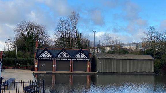A calm lake area with boat sheds in the background.