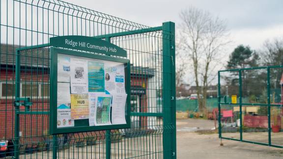 Noticeboard on green fencing reading 'Ridge Hill Community Hub' and posters advertising activities at the hub