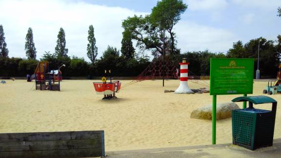 A sandy area in a parkland, with play equipment.