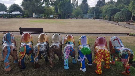 Eight uniquely painted lion sculptures with a bowls green in the background.