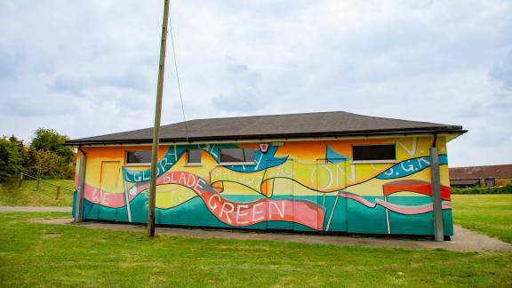 One-storey building painted yellow and turquoise green with a red banner reading 'Slade Green'