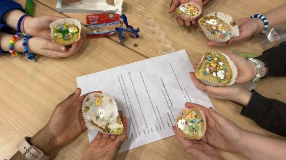 Looking down onto a people's hands on a table, with each person holding out a small iced cake.