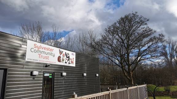 A single-storey building behind railings, with a banner reading 'Sylvester Community Trust'.