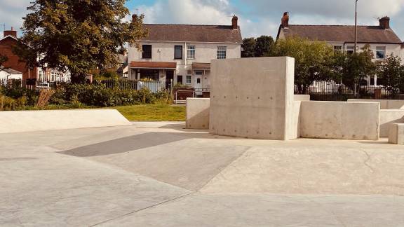 A concrete plaza area with sculptural concrete blocks in the centre, and suburban housing in the background.