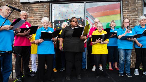 A choir in colourful polo shirts singing, with each person holding an open music folder.