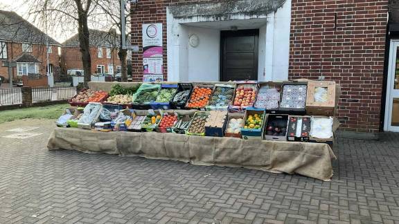 A well-stocked fruit and vegetable stall in front of a red-brick building.
