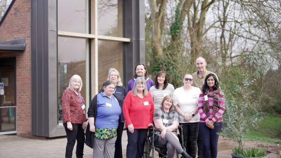 A group of people smiling at the camera outside a modern red-brick building with large windows.