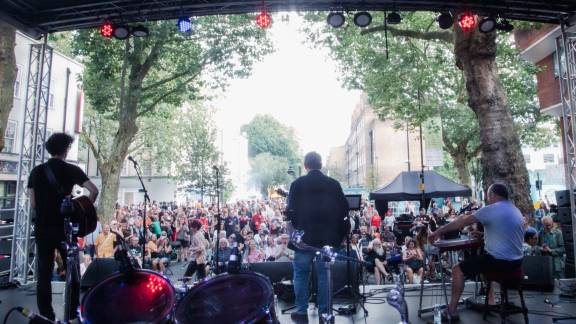 A photo of a large crowd taken from behind the members of a band on an outside stage.