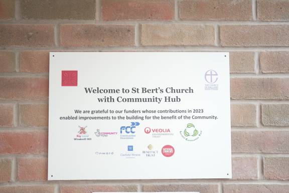 A metal sign on a wall reads: "Welcome to St Bert's Church with Community Hub"