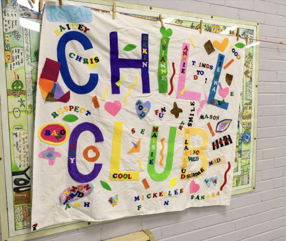 A colourful tapestry with letters reading "Chill Club" is hung on a white wall.