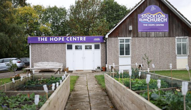 A grey pebble dashed building with a sign reading 'The Hope Centre: Stockton Elm Church' with raised plant beds outside.
