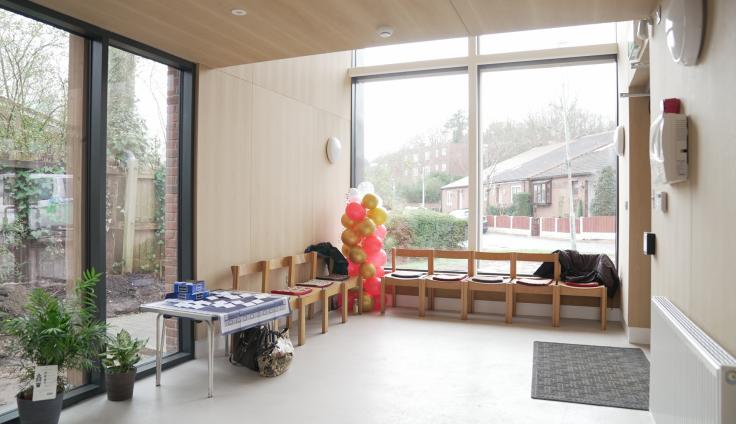 A bright room with chairs and large windows, balloons and plants.