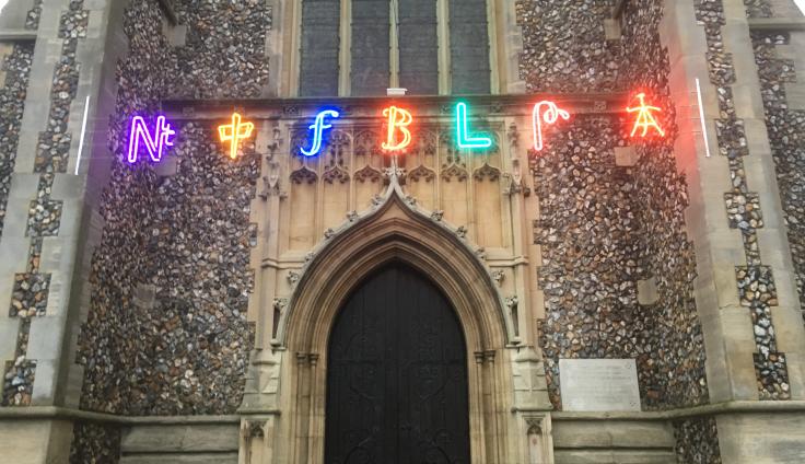 Multi-coloured lights hung over the entrance of a church, with the letters F B L in the centre.