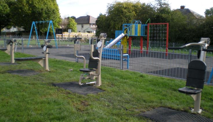 A playground with climbing frames adjacent to a row of outside gym equipment.