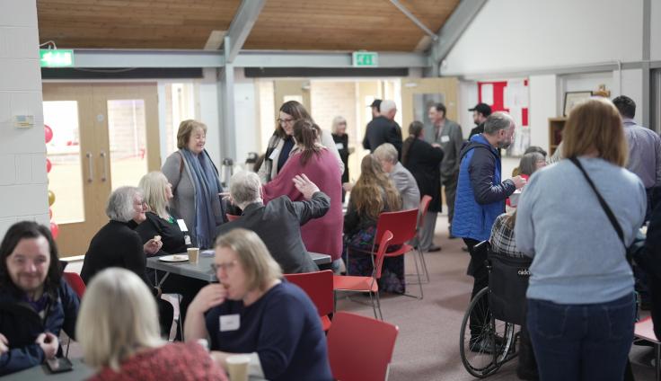 Groups of people sitting at a table talking and people standing in groups in the background