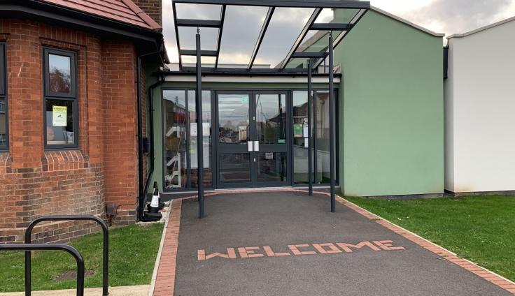 A single-storey red-brick building with a tarmacked path and glass door entrance.