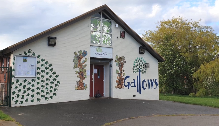 A single-storey community centre with trees behind, with murals and the word 'Gallows' painted on the front elevation.