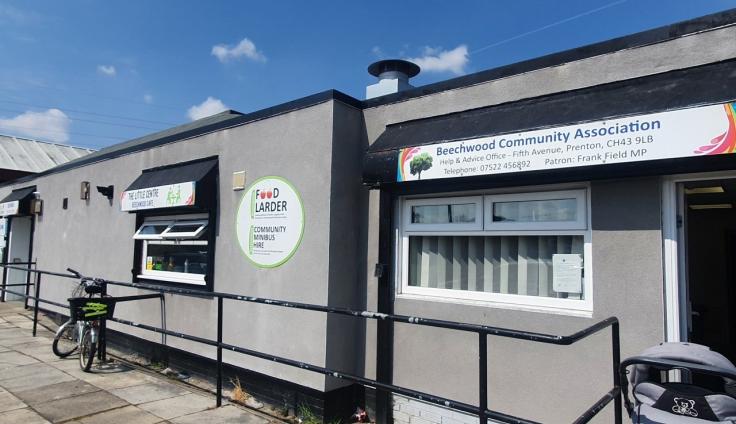 A single-story grey building behind hand-railings, with signs for 'Food larder' and 'Beechwood Community Association'.