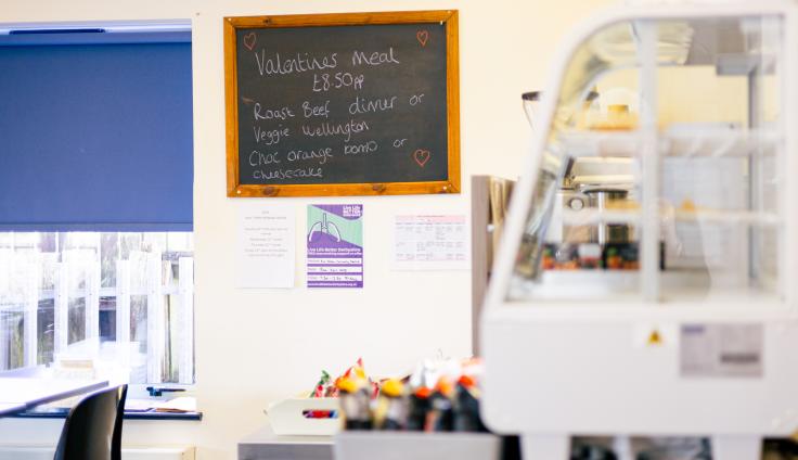 A blackboard on the wall with a small white display case for cakes.