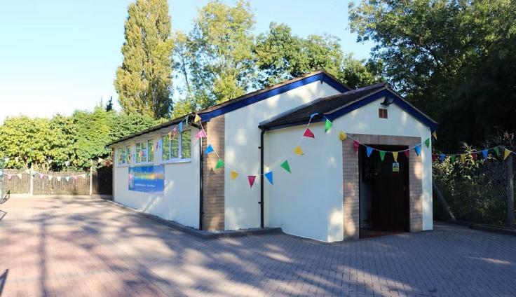 A single-storey cream rendered building with trees behind, adorned with colourful bunting.