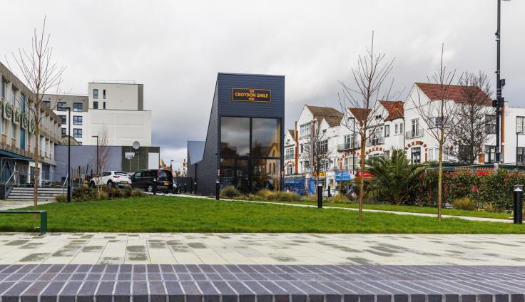 A modern glass-fronted building with a grassed area and paving in front.