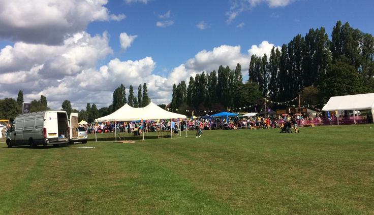 A large field on a sunny day with white tents and lots of people, including some dogs.