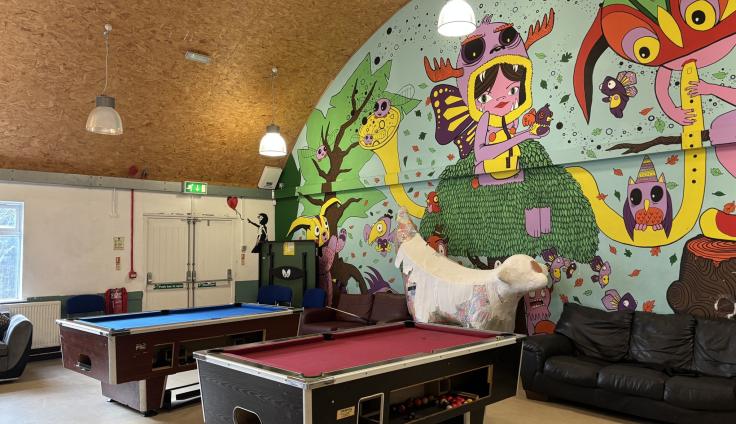 A large room with a colourful mural on one wall and two pool tables.