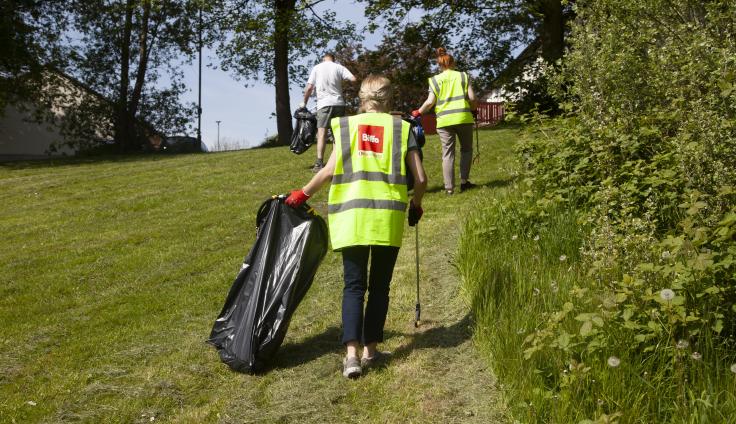 Three adults collecting litter on a green suburban hillside.