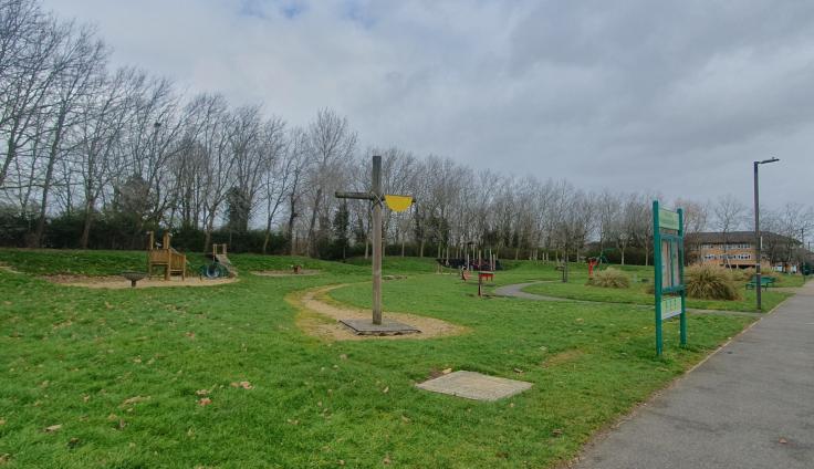 An open park area with play equipment and a large wooden cross.