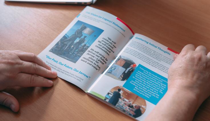Someone holding a colourful booklet open on a table.