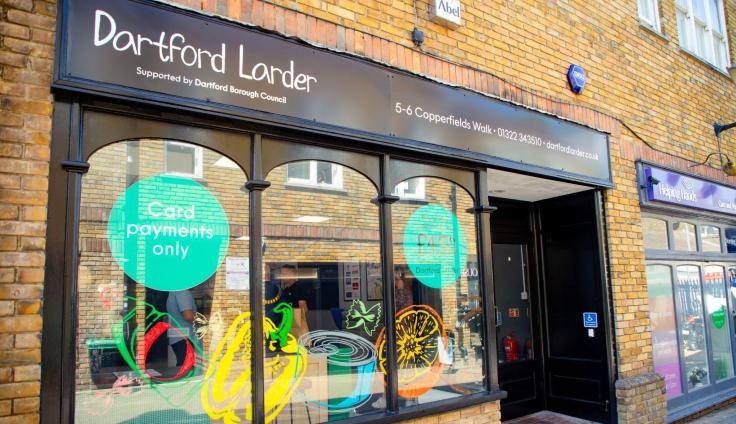 A shop front with arched windows in a red-brick building, below a sign reading Dartford Larder.