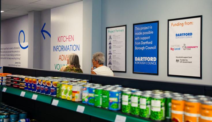 A shelf full of canned goods in the foreground and two women walking away from the camera in the background.