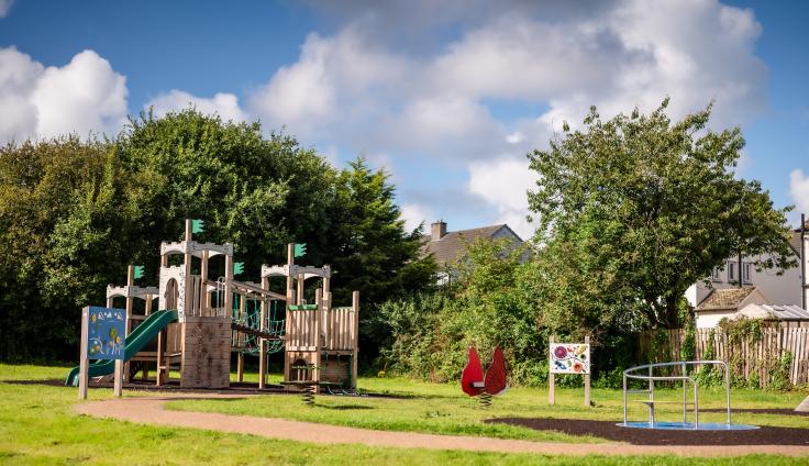 Wooden playground equipment including a slide and red spring rocker in a green area.