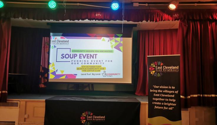 The front stage of a hall showing a projected PowerPoint slide reading 'Soup Event'.