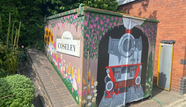 A colourful mural on a storage container showing a steam train and flowers and a sign that reads 'Welcome to Coseley'.