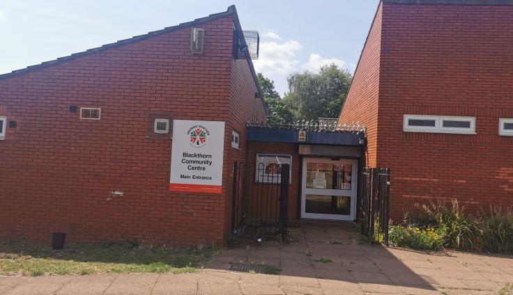 Red brick building with sloping roof and a sign that reads 'Blackthorn Community Centre: Main Entrance'.