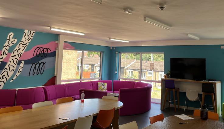 A brightly-decorated room with a mural on the wall, red seating and a media wall.