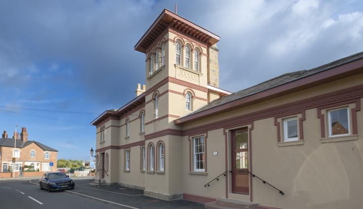 A peach coloured one-storey building of Italianate design with a three-storey tower in the centre