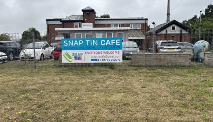 A two-storey red bricked building with grass outside and a large sign reading 'Snap Tin Cafe'