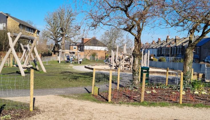 Wooden playground equipment on a grassed area with bare winter trees and a blue sky.